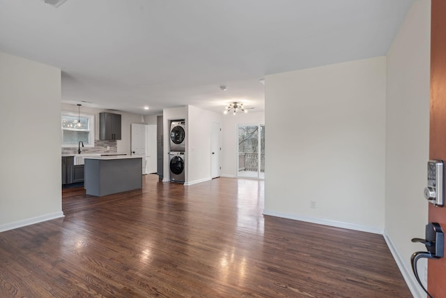 unfurnished living room featuring dark wood finished floors, stacked washer and clothes dryer, and baseboards