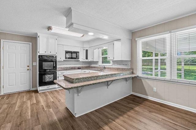 kitchen with sink, a kitchen breakfast bar, kitchen peninsula, white cabinets, and black appliances