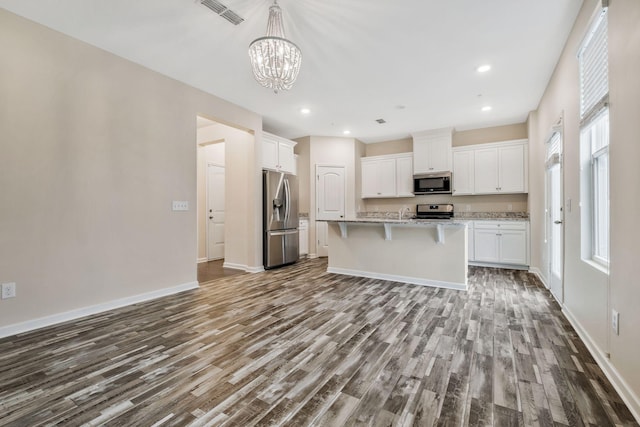 kitchen featuring appliances with stainless steel finishes, hardwood / wood-style floors, white cabinetry, an island with sink, and a kitchen bar