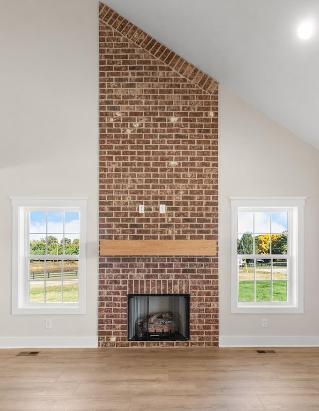 unfurnished living room featuring high vaulted ceiling, a brick fireplace, and light wood-type flooring