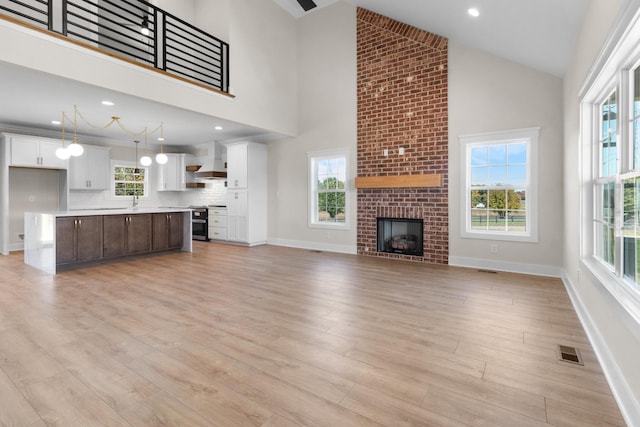 unfurnished living room with high vaulted ceiling, a fireplace, and light wood-type flooring