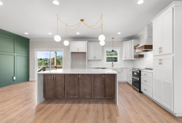 kitchen with a kitchen island, decorative light fixtures, white cabinetry, range with two ovens, and custom exhaust hood