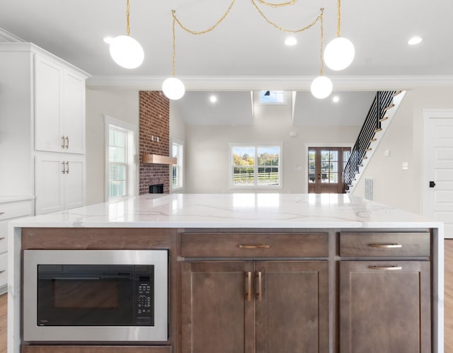 kitchen featuring built in microwave, white cabinetry, crown molding, hanging light fixtures, and a fireplace