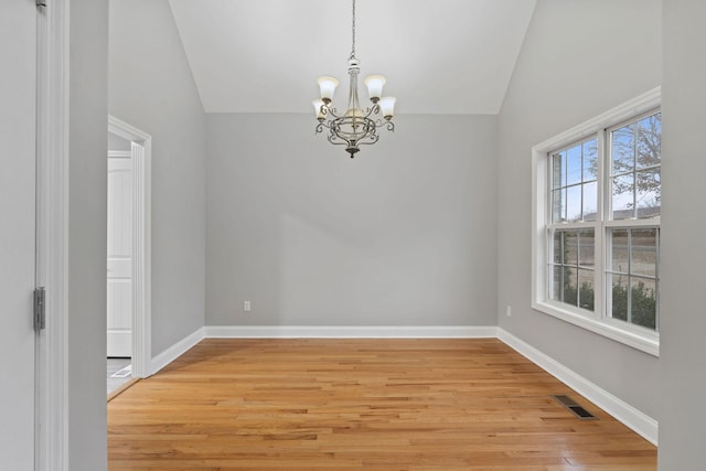 spare room featuring lofted ceiling, a chandelier, and light wood-type flooring