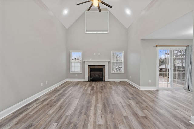 unfurnished living room with ceiling fan, high vaulted ceiling, light hardwood / wood-style floors, and a tile fireplace