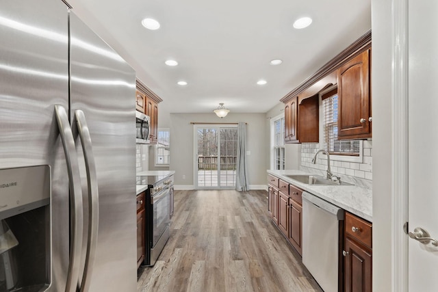 kitchen featuring sink, light stone counters, stainless steel appliances, light hardwood / wood-style floors, and decorative backsplash