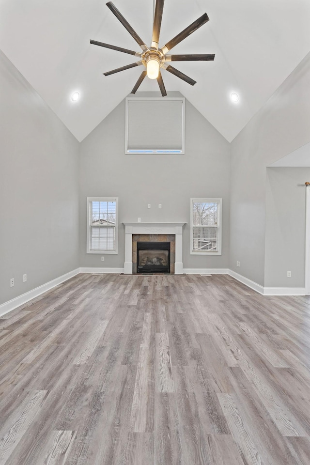 unfurnished living room with a tiled fireplace, high vaulted ceiling, light hardwood / wood-style floors, and ceiling fan