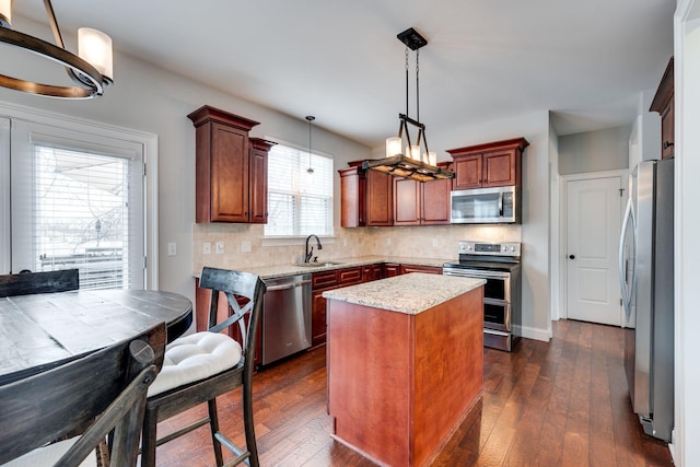 kitchen featuring pendant lighting, sink, appliances with stainless steel finishes, dark hardwood / wood-style floors, and a center island