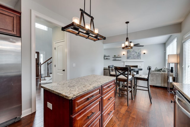 kitchen featuring decorative light fixtures, dark hardwood / wood-style floors, a kitchen island, stainless steel appliances, and light stone countertops