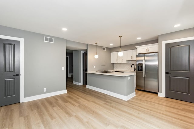 kitchen with stainless steel refrigerator with ice dispenser, white cabinetry, light wood-type flooring, an island with sink, and pendant lighting