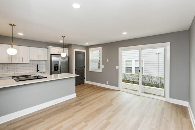 kitchen featuring pendant lighting, stainless steel refrigerator with ice dispenser, tasteful backsplash, light hardwood / wood-style floors, and white cabinets