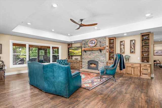 living room featuring a fireplace, dark hardwood / wood-style flooring, ceiling fan, a tray ceiling, and built in shelves