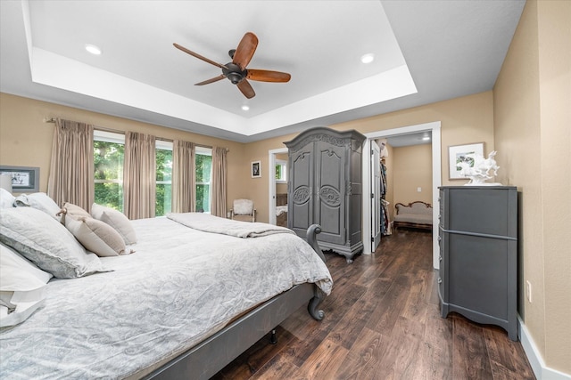 bedroom with a raised ceiling, dark wood-type flooring, and ceiling fan