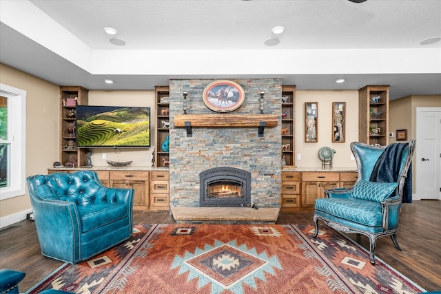 living room with a stone fireplace, dark hardwood / wood-style floors, a textured ceiling, and built in shelves