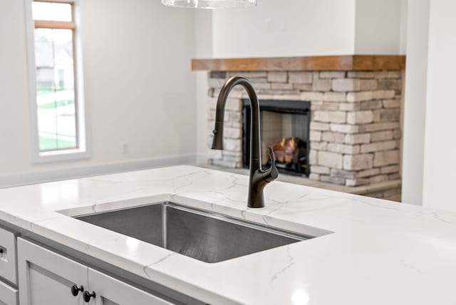 details with a stone fireplace, light stone counters, a sink, and white cabinetry