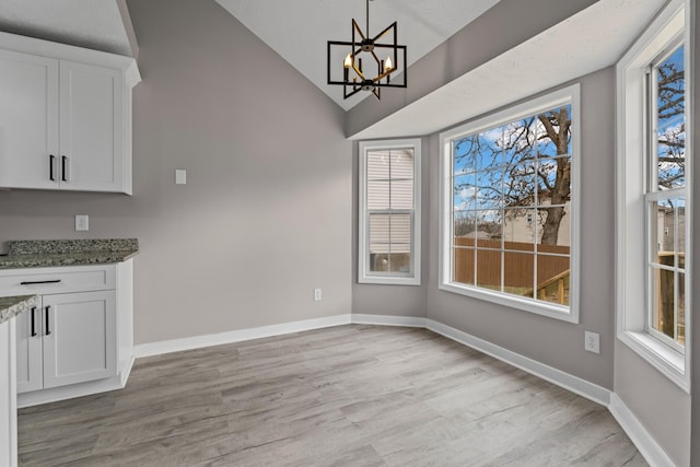 unfurnished dining area featuring lofted ceiling, light hardwood / wood-style flooring, and an inviting chandelier