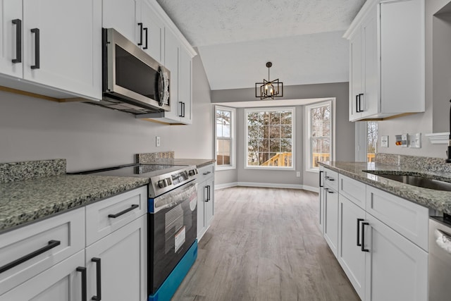 kitchen with lofted ceiling, appliances with stainless steel finishes, light stone countertops, light hardwood / wood-style floors, and white cabinets