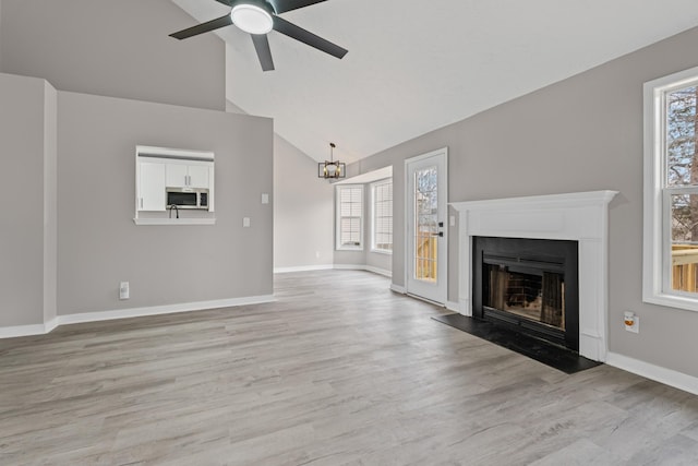 unfurnished living room with ceiling fan with notable chandelier, lofted ceiling, a wealth of natural light, and light wood-type flooring