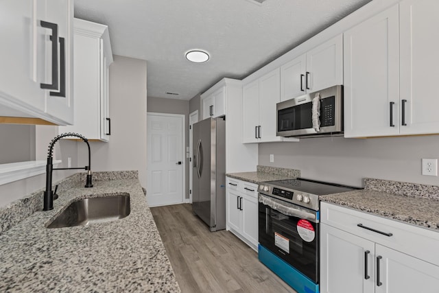 kitchen featuring stainless steel appliances, light stone countertops, sink, and white cabinets