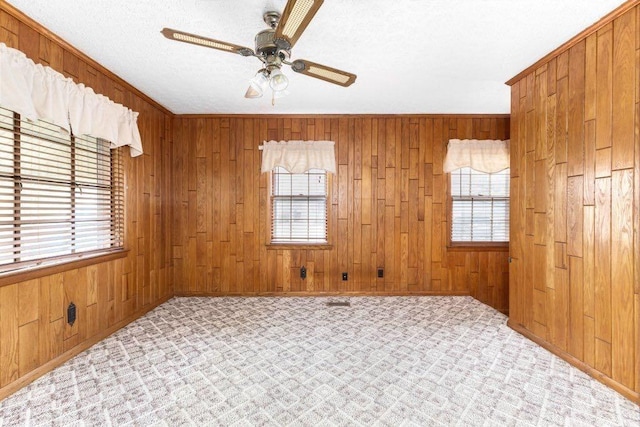 unfurnished room featuring ornamental molding, a healthy amount of sunlight, ceiling fan, and wood walls