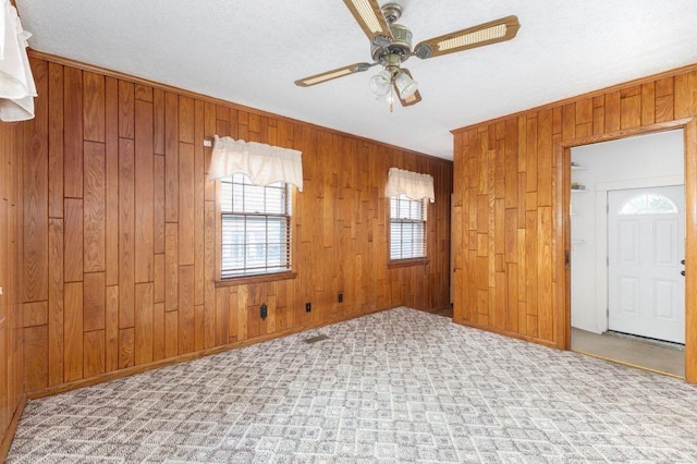 carpeted empty room featuring wooden walls and ceiling fan