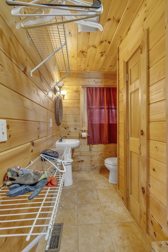 bathroom with toilet, sink, wood walls, wooden ceiling, and tile patterned flooring