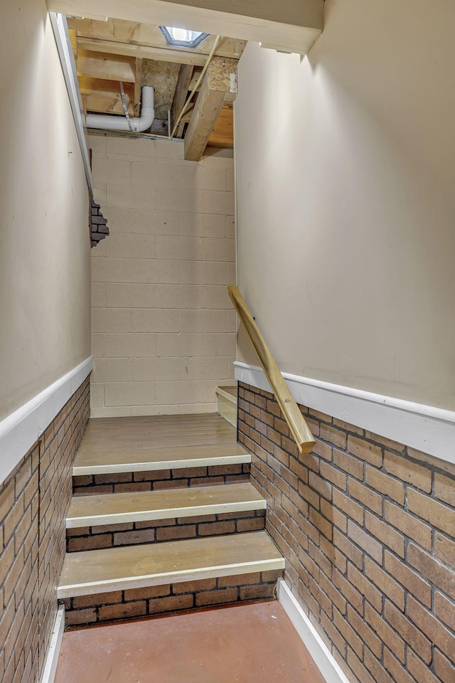 stairs featuring brick wall and concrete floors