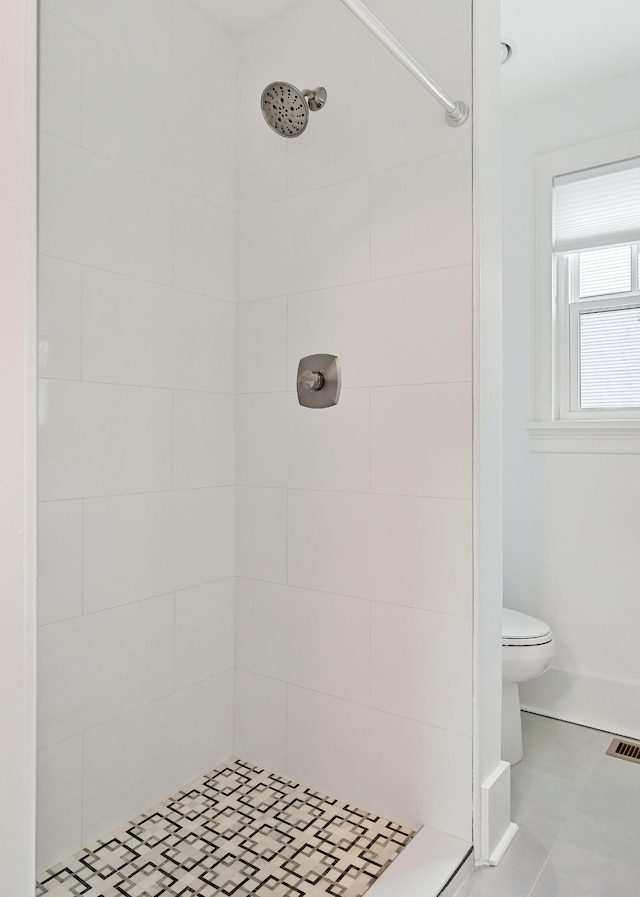 bathroom featuring a tile shower, tile patterned flooring, and toilet