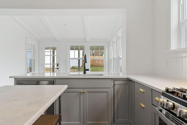 interior space featuring stainless steel gas range oven, sink, beam ceiling, and gray cabinets