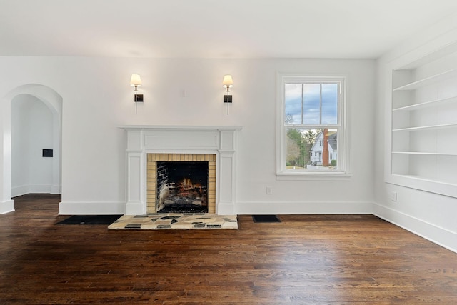 unfurnished living room with built in shelves, a fireplace, and dark wood-type flooring