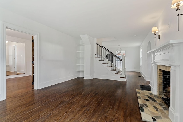 unfurnished living room with dark hardwood / wood-style flooring, a chandelier, and a brick fireplace