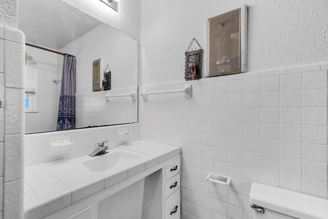 bathroom featuring walk in shower, vanity, toilet, and tile walls