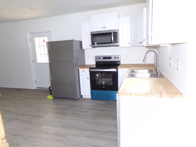 kitchen featuring sink, butcher block counters, stainless steel appliances, light hardwood / wood-style floors, and white cabinets