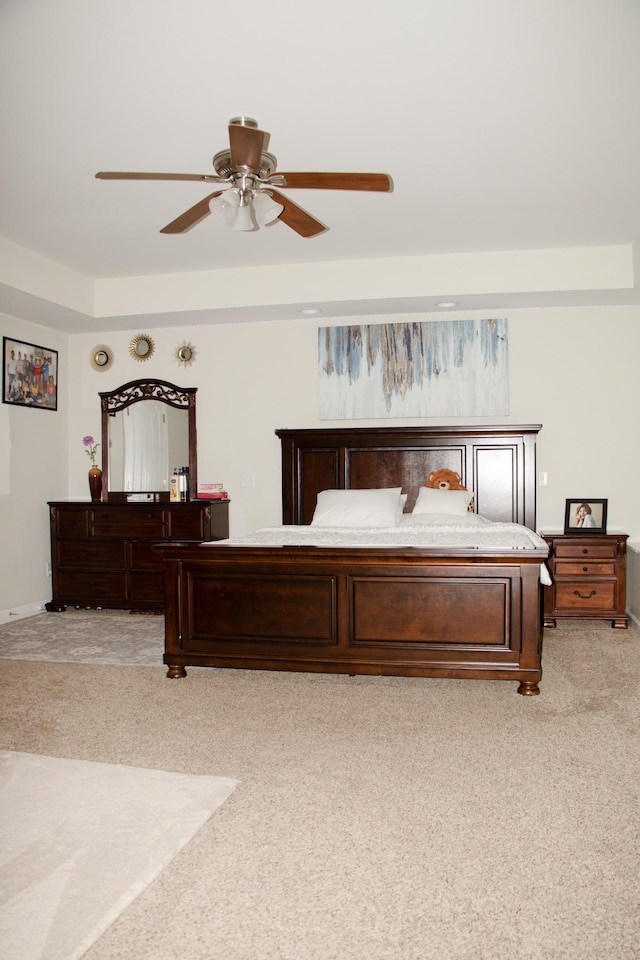 bedroom with light colored carpet, ceiling fan, and a tray ceiling