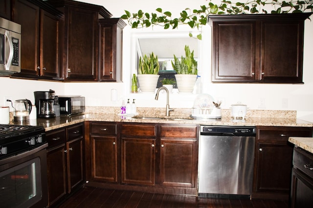 kitchen featuring appliances with stainless steel finishes, sink, dark hardwood / wood-style flooring, dark brown cabinetry, and light stone countertops