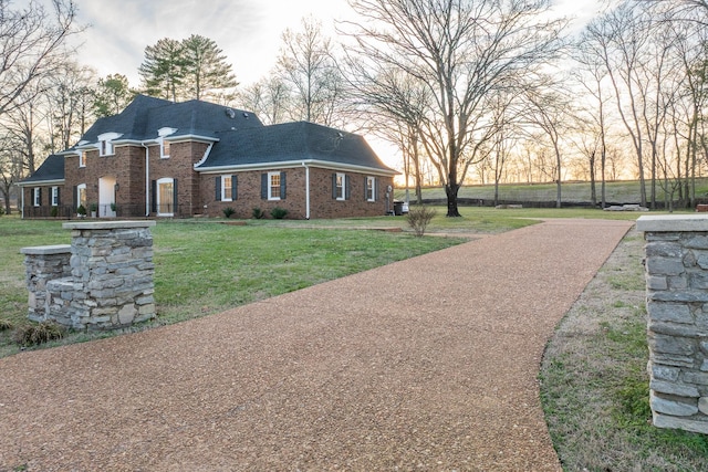 view of front of house with roof with shingles, brick siding, and a front lawn