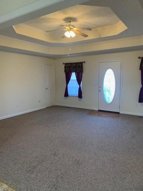 carpeted foyer featuring ceiling fan, ornamental molding, a raised ceiling, and a healthy amount of sunlight