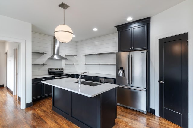 kitchen with pendant lighting, an island with sink, sink, stainless steel appliances, and wall chimney range hood