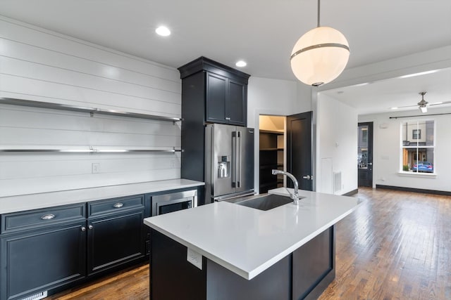 kitchen with dark wood-type flooring, sink, hanging light fixtures, stainless steel appliances, and a kitchen island with sink