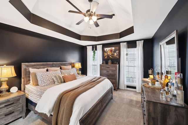 bedroom featuring a raised ceiling, light colored carpet, and ceiling fan