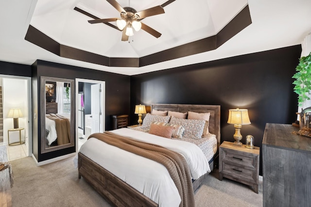 carpeted bedroom featuring a tray ceiling, ensuite bath, and ceiling fan