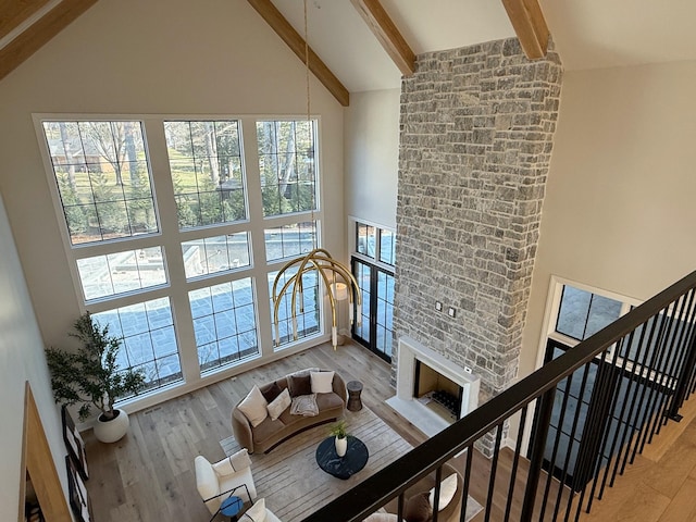 living room featuring beam ceiling, a stone fireplace, high vaulted ceiling, and hardwood / wood-style flooring