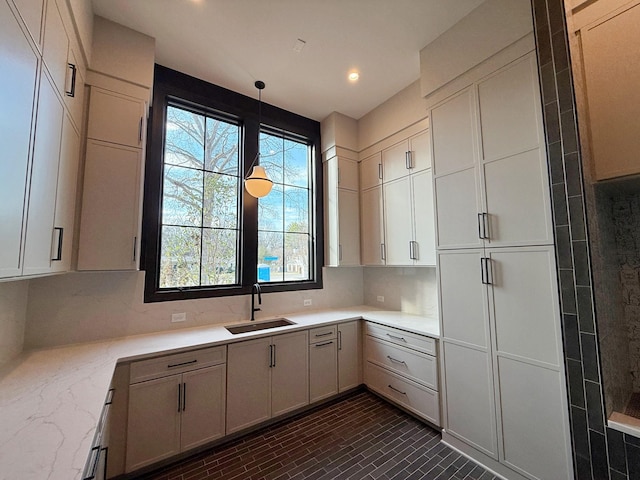 kitchen featuring pendant lighting, sink, white cabinetry, and light stone countertops