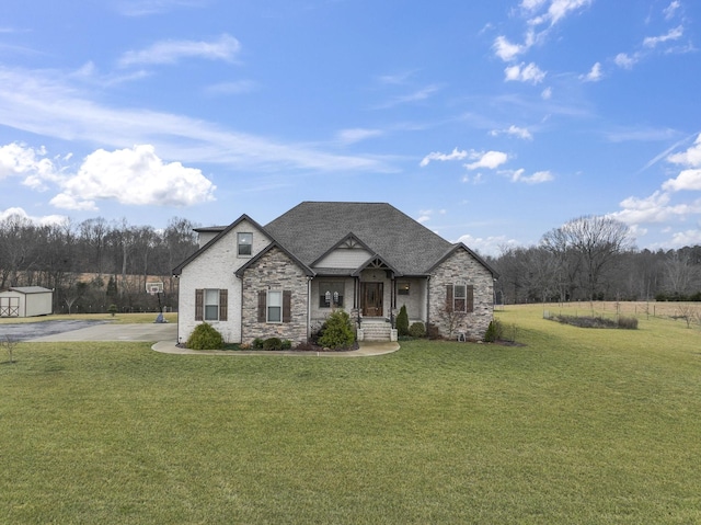 french country inspired facade with an outbuilding, stone siding, a shingled roof, and a front lawn