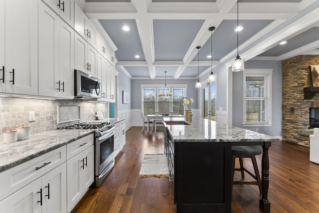 kitchen with coffered ceiling, a breakfast bar, a sink, appliances with stainless steel finishes, and beamed ceiling