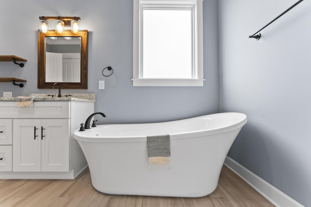 full bath with a soaking tub, vanity, baseboards, and wood finished floors