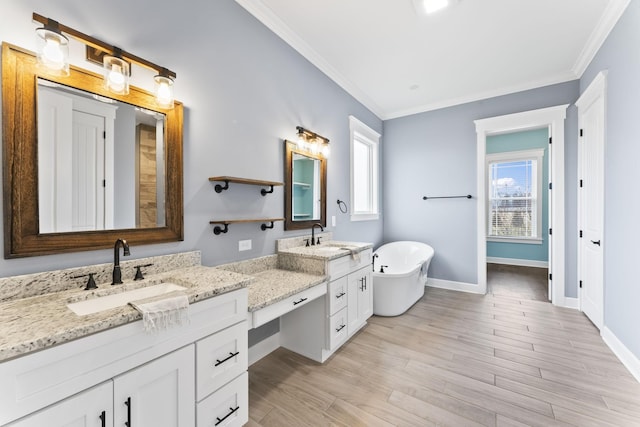 full bath featuring vanity, wood finished floors, baseboards, a freestanding bath, and ornamental molding