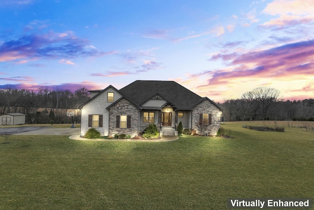 french country inspired facade with a lawn, stone siding, a storage shed, an outdoor structure, and concrete driveway