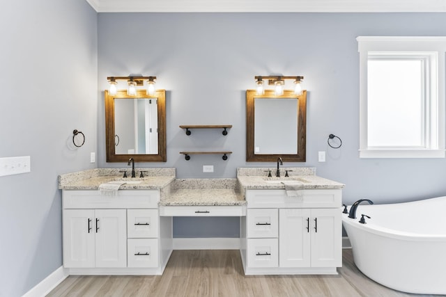 bathroom with a sink, a freestanding tub, two vanities, and wood finished floors