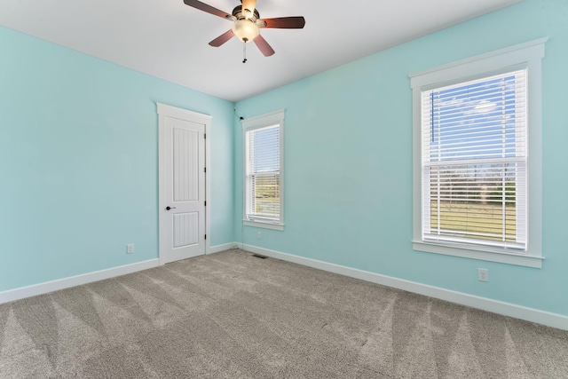 carpeted empty room featuring visible vents, a ceiling fan, and baseboards
